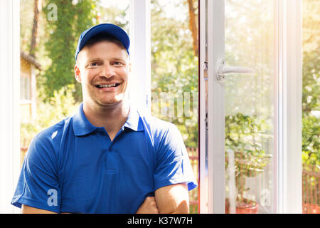 Lächelnd Fenster Installer im blauen Uniform stehen im Zimmer Stockfoto