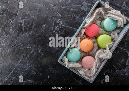 Klassische französische bunte Makronen Cookies in einer Holzkiste auf einem schwarzen konkreten Hintergrund Stockfoto