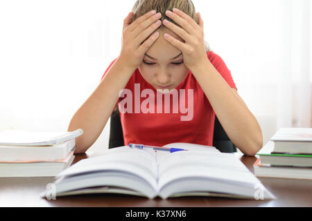 Schülerin hält ihren Kopf in ihre Hände über einen Stapel Bücher auf dem Schreibtisch und ist müde und mit den Hausaufgaben Problem in der Schule frustriert. Stockfoto