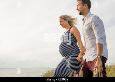 Schwangere Frau am Strand mit Ehemann Spaß Stockfoto