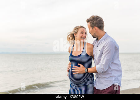Schwangere Frau am Strand mit Ehemann Spaß Stockfoto