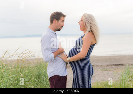 Schwangere Frau am Strand mit Ehemann Spaß Stockfoto