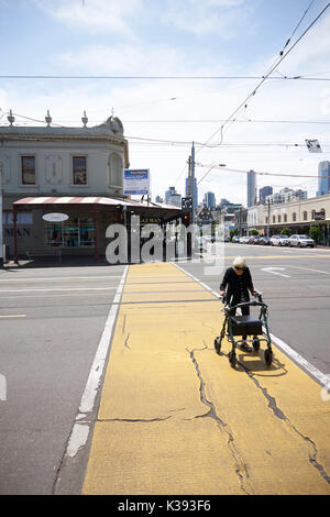 Alte Frau mit einem Walker überquert eine breite Straße in Melbourne, Australien Stockfoto