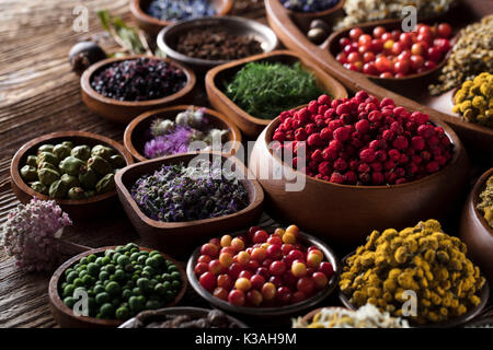 Natürliche Medizin. Kräuter, Beeren und Blumen in Schalen auf hölzernen Tisch. Stockfoto