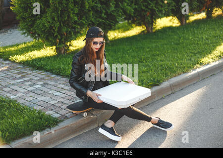 Junge Frau - Teenager mit Skateboard ausruhen und Pizza zum Mitnehmen im Freien zu essen Stockfoto