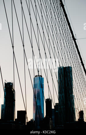 Skyline von Manhattan in der Dämmerung mit dem One World Trade Center nicht nur aus, sondern durch die Leitungen der Brooklyn Bridge. Stockfoto