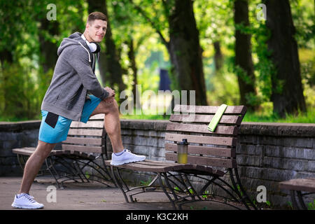 Ein Foto der jungen, gutaussehenden Mann trainieren auf der Bank im Park. Stockfoto
