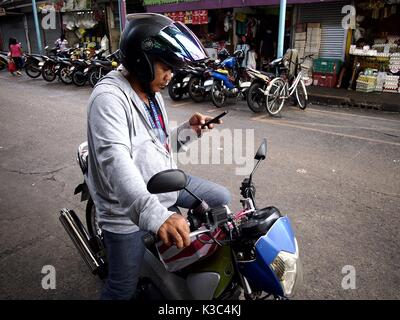 MARIKINA CITY, Philippinen - 28. AUGUST 2017: Ein Motorradfahrer hält an einem Bürgersteig auf eine Nachricht auf sein Handy prüfen. Stockfoto