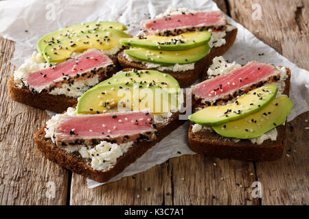 Köstliche Sandwiches mit gebratenen Thunfisch, Sesam, Avocado und Hüttenkäse close-up auf dem Tisch. Horizontale Stockfoto