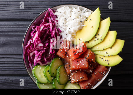 Hawaiian tuna poke Schüssel mit Avocado, Rotkohl, Gurken und Sesam auf schwarzem Holz- Hintergrund. Draufsicht von oben horizontal Stockfoto