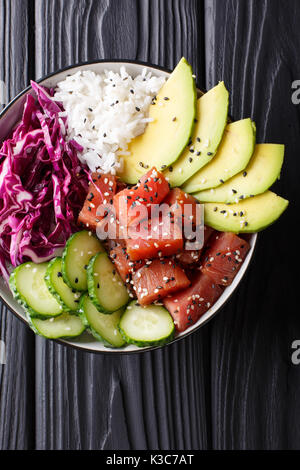 Hawaiian tuna poke Schüssel mit Avocado, Rotkohl, Gurken und Sesam auf schwarzem Holz- Hintergrund. Draufsicht von oben vertikal Stockfoto