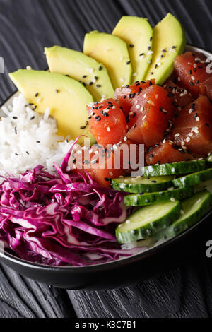 Hawaiian tuna poke Schüssel mit Avocado, Rotkohl, Gurken und Sesam auf schwarzem Holz- Hintergrund. Vertikale Stockfoto