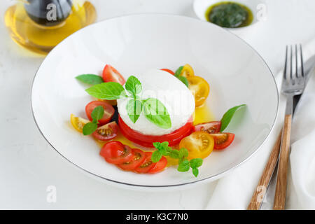 Caprese Salat mit roten und gelben Tomaten, Mozarella, Basilikum und Olivenöl. Ansicht schließen. Weißer Hintergrund Stockfoto