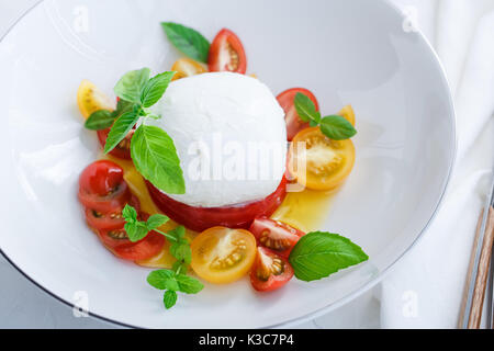 Caprese Salat mit roten und gelben Tomaten, Mozarella, Basilikum und Olivenöl. Ansicht schließen. Weißer Hintergrund. Stockfoto