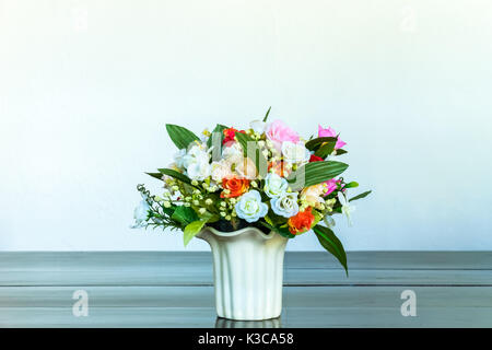 Vase mit künstlichen Rose auf Holzbank mit weißen Wand Hintergrund Stockfoto