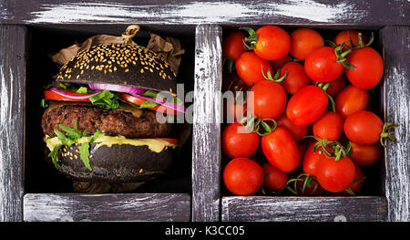 Schwarz big Sandwich - schwarz Hamburger mit saftigen Beef Burger, Käse, Tomaten und rote Zwiebel in Feld auf schwarzem Hintergrund. Flach. Ansicht von oben Stockfoto