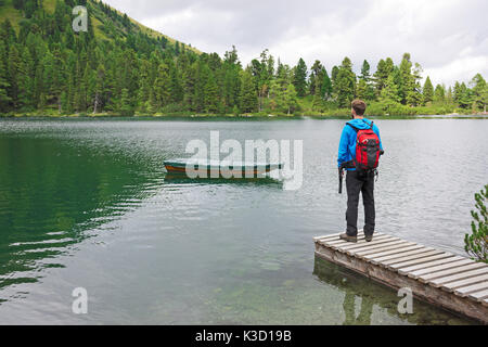 Man steht auf einem Steg an einem wunderschönen einsamen Bergsee, in einem Ruderboot auf türkisfarbenen kristallklaren Wasser suchen, von Wald umgeben. Stockfoto