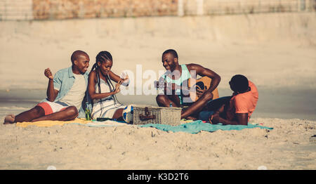 Gruppe junger Leute am Strand hängen. Junge afro-amerikanische Mann spielt Gitarre für Freunde. Stockfoto