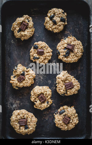 Frisch gebackene Haferflocken Rosinen Cookies mit dunklen Schokolade, Zimt und Nüsse auf alten rostigen Plätzchenblatt. table top Aussicht, vertikalen Zusammensetzung Stockfoto