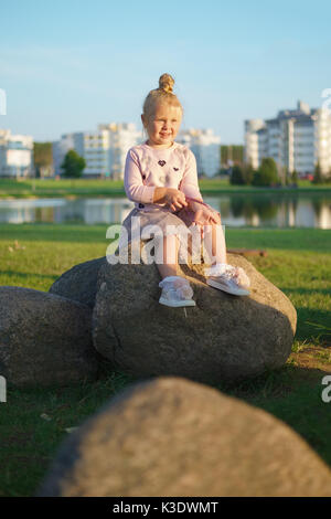 Kleines Mädchen sitzen auf Stein im Sonnenuntergang Stockfoto