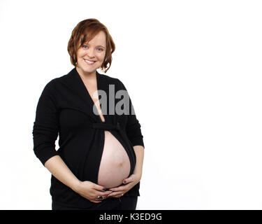 Junge schwangere Frau Lächeln für die Kamera, während Bauch Holding im Studio Stockfoto