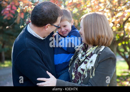 Mutter, Vater und Sohn in eine Umarmung und gemeinsam Lachen in der Landschaft im Herbst. Stockfoto