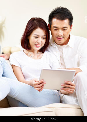 Asiatische Paar auf die Verwendung digitaler tablet Couch zusammen zu Hause sitzen. Stockfoto