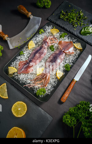 Frische Tintenfische mit Eis und Zitrone auf schwarze Platte Stockfoto