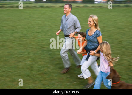 Junge Familie läuft Hand in Hand über einer Wiese Stockfoto