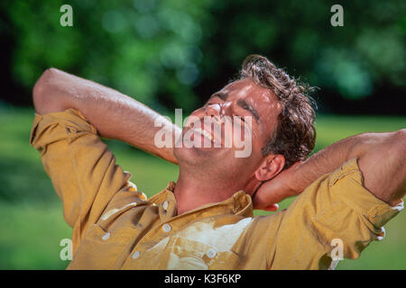 Mann an der Augen kreuzt die Arme hinter dem Kopf Stockfoto