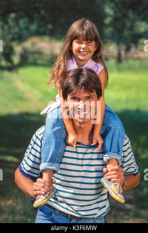 Vater trägt Lachen Tochter mit braunen langen Haaren auf den Schultern Stockfoto