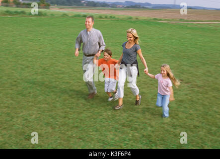 Junge Familie läuft Hand in Hand über einer Wiese Stockfoto