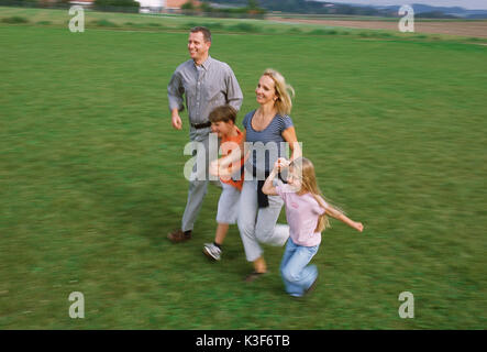 Junge Familie läuft Hand in Hand über einer Wiese Stockfoto