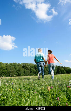 Junges Paar läuft Hand in Hand über einer Wiese Stockfoto
