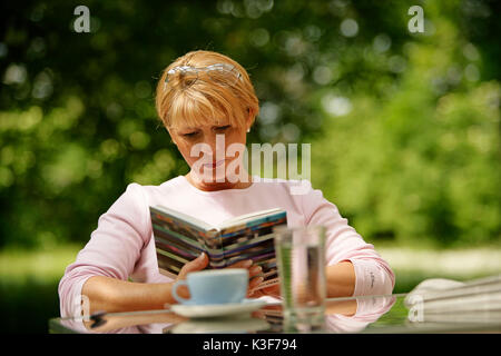 Frau sitzt im Garten und liest Stockfoto