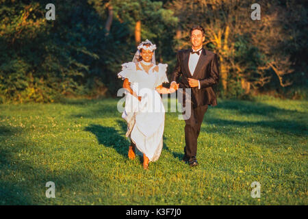 Braut und Bräutigam läuft Hand in Hand über einer Wiese Stockfoto