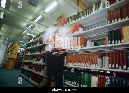 Der Mensch trägt Buch los in einer Bibliothek Stockfoto