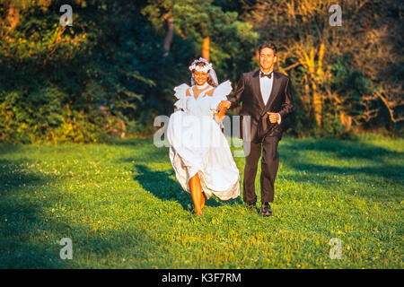 Braut und Bräutigam läuft Hand in Hand über einer Wiese Stockfoto