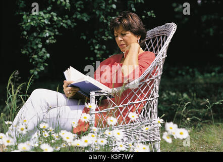 Frau sitzt im Garten und liest Stockfoto