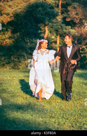 Braut und Bräutigam läuft Hand in Hand auf einer Wiese entlang Stockfoto