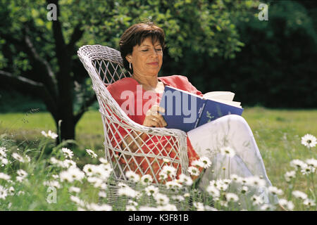 Frau sitzt im Garten und liest Stockfoto