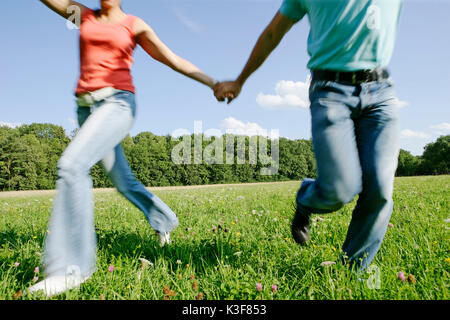 Junges Paar läuft Hand in Hand über einer Wiese Stockfoto