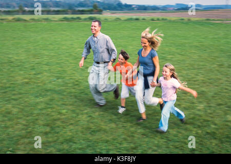 Junge Familie läuft Hand in Hand über einer Wiese Stockfoto