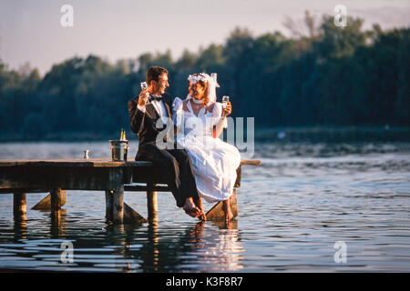 Brautpaar sitzt auf der Brücke mit Champagner Glas in der Hand Stockfoto