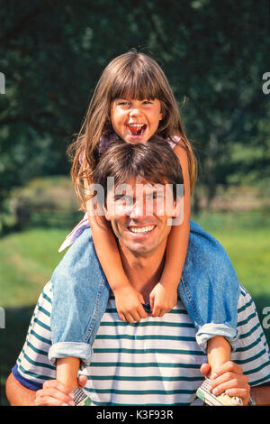 Vater trägt Lachen Tochter mit braunen langen Haaren auf den Schultern Stockfoto