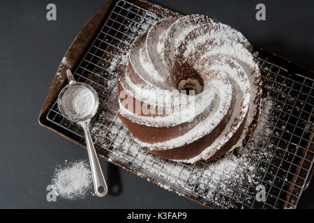 Hohe Betrachtungswinkel von Vanille Bundt Cake bestreut mit Puderzucker und kleinen Sieb Stockfoto