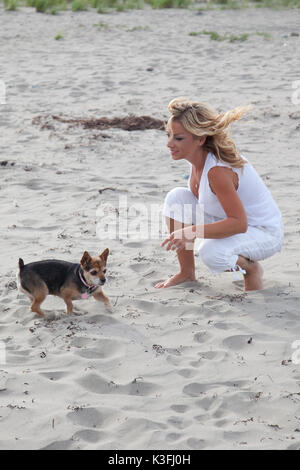 Schöne blonde Frau spielt mit ihrem Hund am Strand Stockfoto