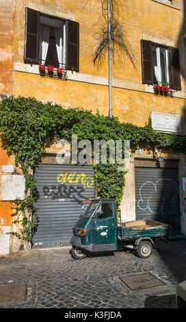 Altes, dunkles Grün Piaggio Ape dreirädrige Nutzfahrzeug vor einer bewachsenen Fassade im historischen Stadtzentrum von Rom geparkt Stockfoto