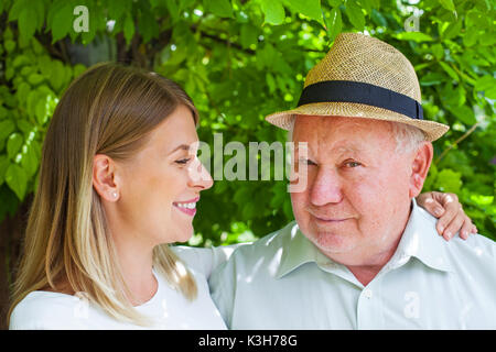 Lächelnd älterer Mann mit schönen jungen Enkelin im Park posing Stockfoto