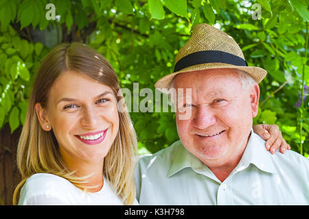 Lächelnd älterer Mann mit schönen jungen Enkelin im Park posing Stockfoto